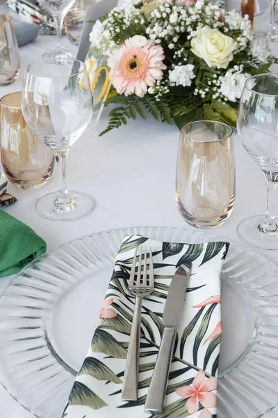 Table arrangement prepared for a formal event, a wedding or a special occasion, decorated with tropical-themed details such as flowers, tablecloths and linen napkins for an enhanced dinner experience