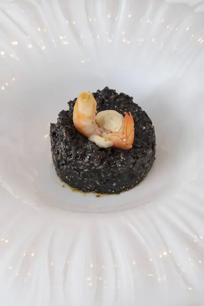 Gourmet seafood dish with black squid ink rice and a succulent shrimp perched atop, culinary experience created with the finest ingredients and a balanced infusion of textures and briny, ocean flavors