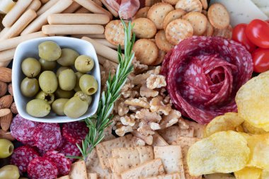 Lezzetli atıştırmalıklar, kraker, ekmek, patates cipsi, salam dilimleri, domates, ceviz ve bir kase yeşil zeytin eşliğinde hazırlandı.