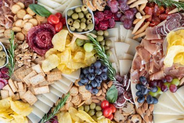 Davet ve iştah açıcı parti yayılımı, çeşitli peynirlerle geniş bir şarküteri kurulu, taze et, taze meyve, fındık ve yeşil zeytin, ekmek çubuğu ve patates cipsi gibi diğer yardımlar
