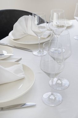 Üzerinde katlanmış peçeteler, el değmemiş masa örtüsü üzerinde şarap bardakları ve gümüş takımlar bulunan büyük beyaz tabaklar güzel bir yemek deneyimi ya da özel bir durum için hazırlanmıştır.
