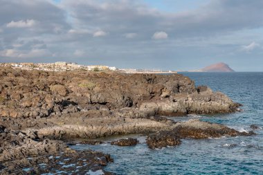 Amarilla Golf Tesisi yakınlarındaki engebeli lav kayaları Golf del Sur ve Los Abrigos köyüne doğru uzanırken, arka planda kırmızı renkli volkanik koni Montana Roja, Tenerife, Kanarya Adaları, İspanya