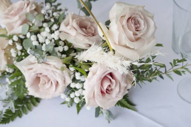 Bir yemek masasının üzerine kurulmuş zarif bir süs. Çiçek aranjmanı. Çiçeklerde, yeşil ve beyaz dolgu çiçekleriyle tamamlanmış pembe güller var.