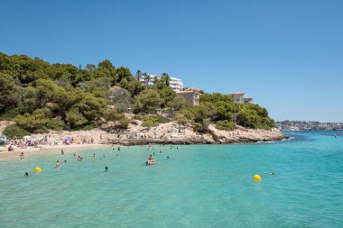 Playa de Illetes, Palma de Mallorca, Balearic Islands, Spain - June 26, 2024: stunning Mediterranean beach with pristine blue water, and tourists enjoying a lively atmosphere by swimming and sunbathing