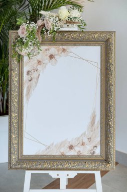 Süslü altın ve bronz çerçeveli klasik bir düğün tabelası, yumuşak pastel çiçekler, beyaz güller, bebek nefesi ve yeşillik ile süslenmiş, selamlama, oturma ve etkinlik detayları için fotokopi alanı