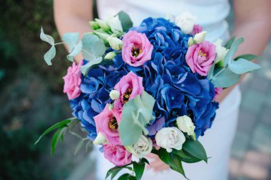 Mavi ortancalar, yumuşak pembe lisianthus çiçekleri, beyaz güller ve bir gelin tarafından tutulan okaliptüs yapraklarından oluşan büyük bir gelin buketinin yakın çekimi, düğün günü için hoş bir çiçek aranjmanı.