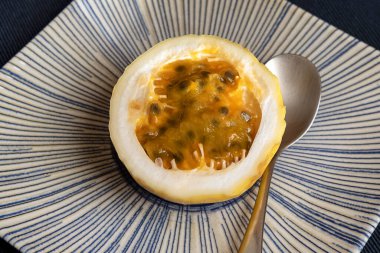 Yarısı tutku meyvesi seramik bir tabakta seramik tohumlarla dolu altın posasını gösteriyor. Mavi desenli, gözü merkeze yönelten ve küçük bir kaşıkla servis edilmeye hazır.