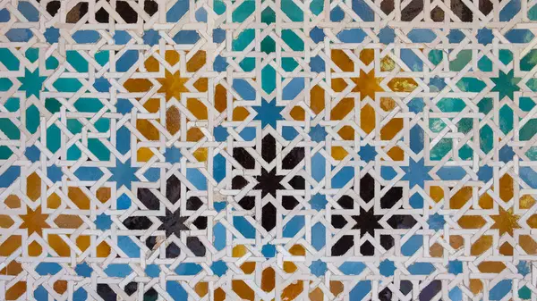Karmaşık geometrik desenlere sahip Endülüs seramik mozaiği, birbirine kenetlenmiş yıldız şekilleri ve mavi, yeşil ve sarı renkli çokgenler, Sevilla, İspanya 'da simetrik bir kompozisyon oluşturur.