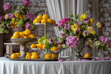 Zarif Masa Sehpaları katmanlı tepsiler üzerine dizilmiş zarif vazolarda canlı pembe ve sarı çiçekler oluşturarak, Limonlar ve Renkli Çiçekler ile özel durumlar için mükemmel bir ahenkli ve taze masa hazırlıyor. Yüksek kalite fotoğraf