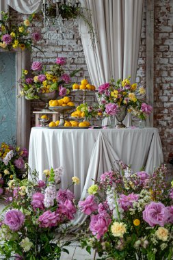 Zarif masa canlı çiçekler ve limonlarla süslenmiş, kırsal bir ortam yaratıyor. Tuğla duvara karşı pembe ve sarı düzenlemeler, şenlikli bir olay olduğunu gösteriyor.