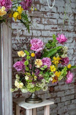 Pembe güllerle canlı çiçek aranjmanı, kırsal tuğla duvara karşı metal bir vazoda sarı ve beyaz çiçekler. Ev dekorasyonu, düğünler ve etkinlikler için mükemmel.