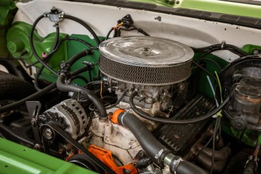 Hava filtresi ve alternatör gibi görünür bileşenleri olan klasik bir araba motoru kompartımanı. Yeşil ve beyaz arkaplan karmaşık makine ve mekanik kurulumu vurgular