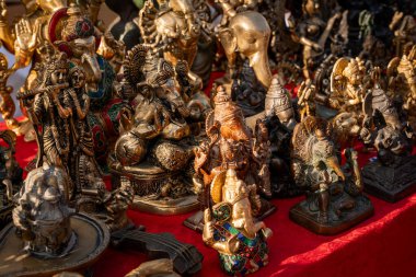 Pirinç rengi Ganesha ve Krishna heykellerinin canlı gösterisi, zengin sanatsal detaylar sergileniyor. Bu geleneksel Hint heykelcikleri bir pazar ortamında kültür işçiliğini ön plana çıkarıyor