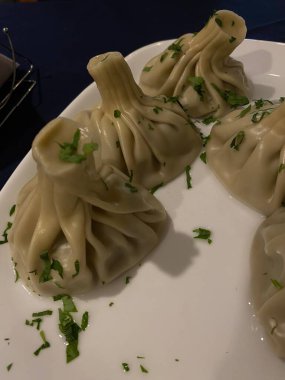 Khinkali beyaz bir tabakta üzerine otlar serpiştirilmiş.