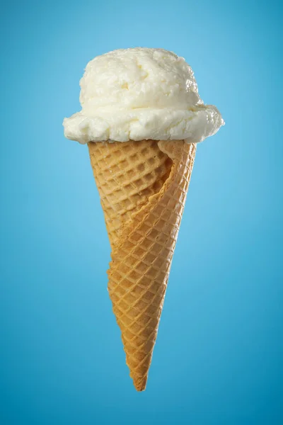 Single ice cream cone with vanilla icecream and a waffle cone on blue background.