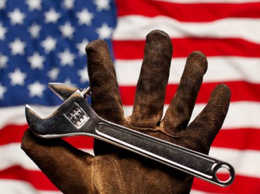 Eski ve yıpranmış iş eldiveni Amerikan bayrağı üzerinde ayarlanabilir anahtarı tutunan,. Amerikan emek, iş ve istihdam kavramı.