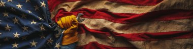 İngiliz anahtarı tutan ve yıpranmış Amerikan bayrağı tutan iş eldiveni. Amerikan yapımı, Amerikan işgücü, mavi yakalı işçi, veya İşçi Bayramı konsepti.