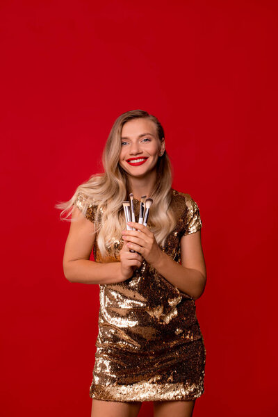 Молодой визажист с кисточками на красном фоне. женщина валяет дурака и держит кисти для макияжа