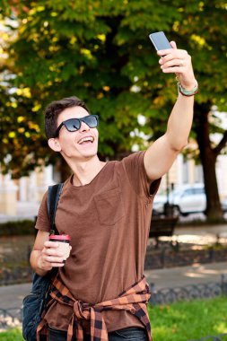 Güneş gözlüğü reklamı, mesaj için yeri olan tişört. Kahverengi tişörtlü genç ve şık bir adam selfie yapıyor.