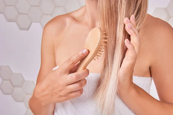 eco natural hair care - blonde woman combs her hair in bathroom. Beauty routine concept