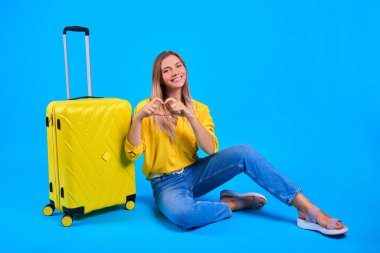 Uzun zamandır beklenen yolculuk konsepti. Aşk seyahati ve yolculuk. Tatil planlıyorum. Mavi arka planda sarı valizli kadın..