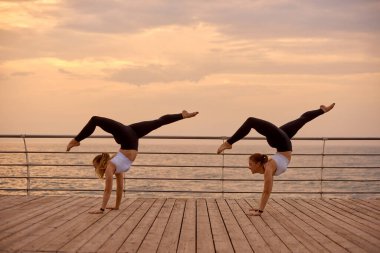 Jimnastikte simetrik element. Spor yapan çift sabah denizde akroyoga, fitness ya da pilates yapıyor.