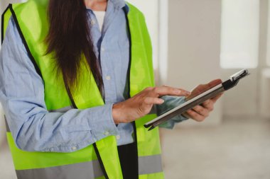 Female Industrial Engineer in High-Visibility Vest Working on Tablet Computer. Inspector or Safety Supervisor in construction site
