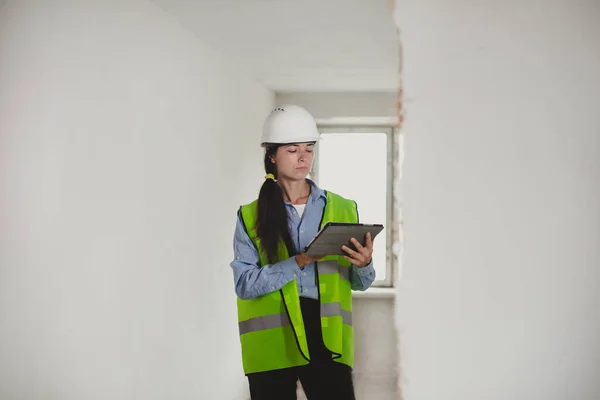 Female Industrial Engineer in White Hard Hat, High-Visibility Vest Working on Tablet Computer. Inspector or Safety Supervisor in construction site