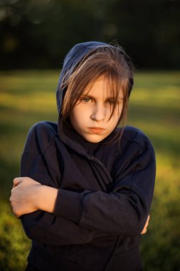 Elleri çapraz gezen mutsuz genç kız akşam üstü yeşil çimlerin üzerinde parkta yürüyor.