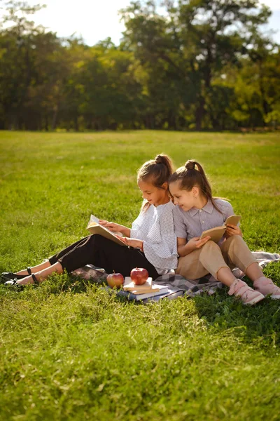 積極的な子供たちの芝生の上で再生に座って 本を読んで 果物を食べる 2人の屈託のない友達が授業後に — ストック写真