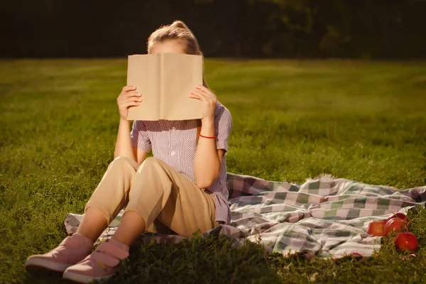 Genç Bir Kız Elinde Kitapla Yüzünde Defterle Parkta Oturuyor — Stok fotoğraf