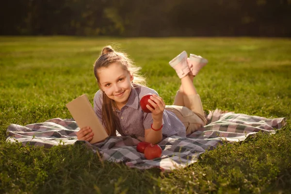 Sorridente Bambina Che Tiene Libro Mela Mano Riposa Nel Parco — Foto Stock