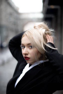 Piercing bakışlı genç bir kadın saçını yağmurdan ve rüzgârdan gizliyor.