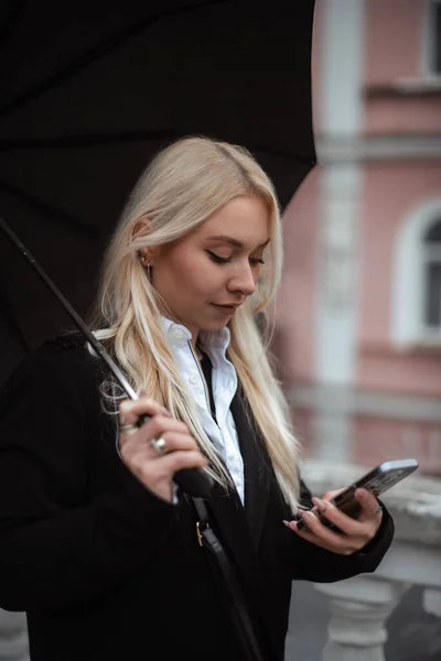 Mujer Joven Usando Teléfono Inteligente Sosteniendo Paraguas Negro Durante Las — Foto de Stock