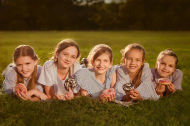 Dünya Çocuk Günü kutlaması. Mutlu kızlar yeşil çimlere uzanıp parkta tatlı çörekler yiyorlar.