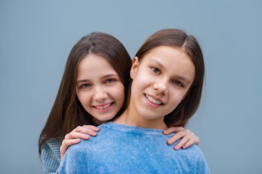 Mavi arka planda kameraya bakıp gülümseyen iki genç kız. Biri renkli diş telli, diğeri de doğru ısırığı almamış.