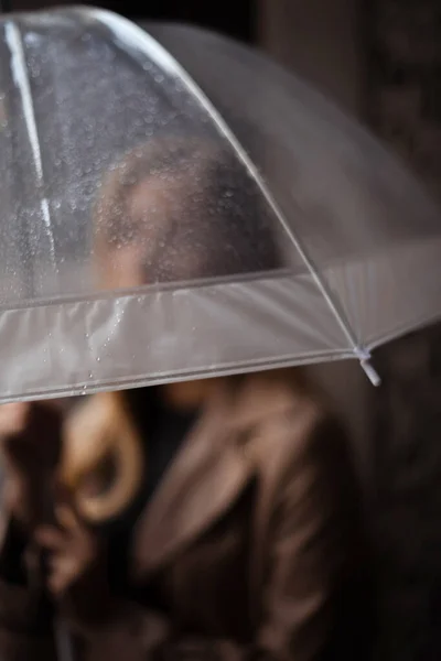 focus on rain drops on transparent umbrella in woman hands in rainy day. Urban solitude in rain