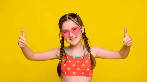 ハートの形をしたピンクのサングラスをかけた女の子が親指を立てて両手でジェスチャー — ストック写真