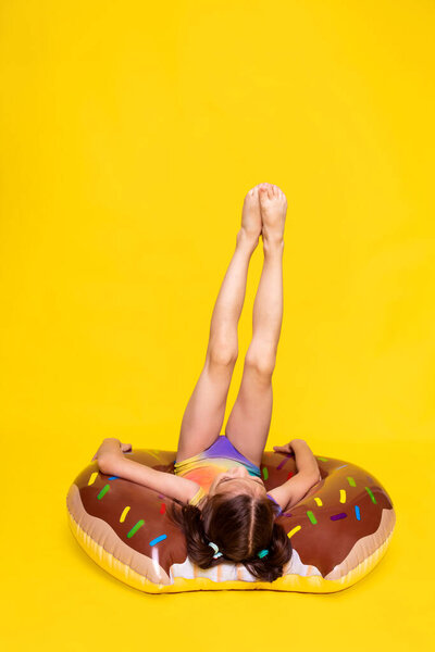 girl in swimsuit lay on inflatable ring and keeps legs up, resting and relaxing in summer