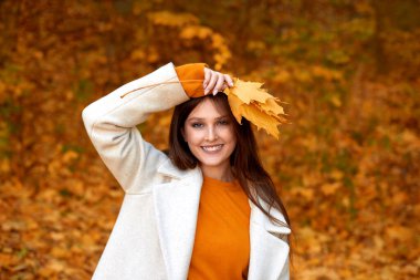 Sonbahar parkında yürüyen mutlu bir kadın, iyi bir ruh hali içinde gülerek ve sonbahar ormanında kameraya bakarak.