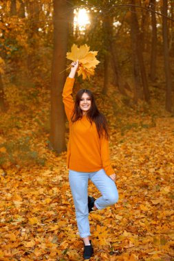Parlak giyimli kadın doğada yürüyor ve atmosferden mutlu sonbahar yaprakları dökülüyor.