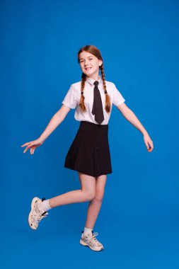 Okul üniformalı kız öğrenci mavi arka planda okula döndüğü için heyecanlı..