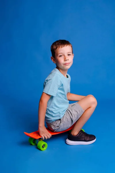 青いモックアップTシャツの男の子は ライトブルーのスタジオの背景の上に隔離されたスケートボードに座って — ストック写真