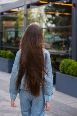 Güzel bakımlı saçlar rüzgârda gelişiyor. Şehir caddesinde yürüyen bir kız üzerinde.