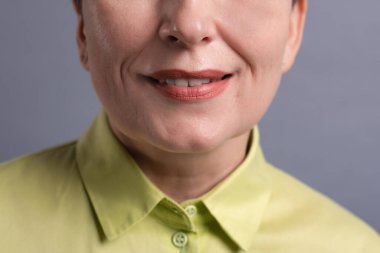 Gri arka planda 50 'li yaşlarda yaşlı bir kadın, kuru cilt bakımı, yaşlanmayı önleyen kozmetik ürünler, estetik cerrahi, kozmetoloji prosedürleri. Yüzün yarısının yakın görüntüsü