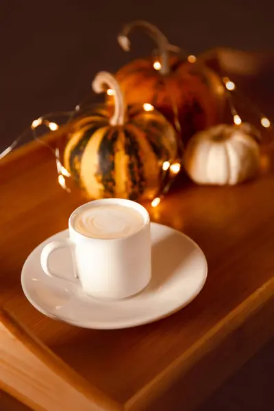 cup of pumpkin coffee on wooden tray with small decorative pumpkins. winter evening holiday mood