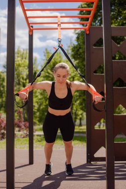 Kadın şınav çekiyor, kollarını eğitiyor dışarıda spor kemerleri takıyor.