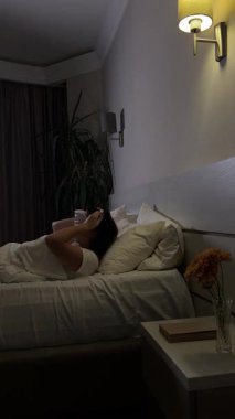 Geceleri yatakta uyku maskesi takan bir kadın. dikey video