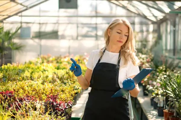 Kadın bahçıvan kağıt tablette kayıt tutuyor seradaki bitkilerle çalışıyor.