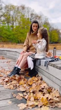 Anne ve kızı sonbaharda sonbahar pikniğinde sıcak çay içiyorlar.